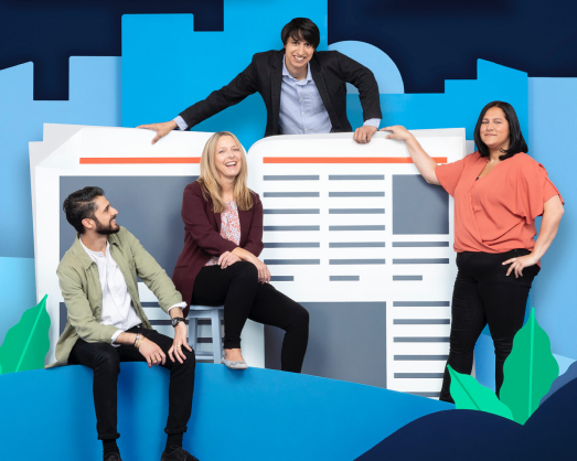 Four coworkers smiling and posing in front of a newspaper